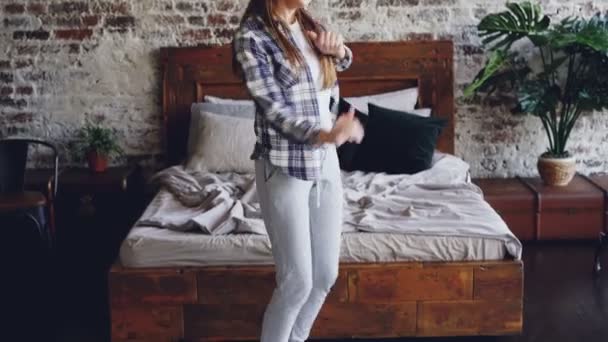 Pretty careless girl in casual clothes is dancing in bedroom and listening to music with wireless headphones. Young people, leisure time and modern lifestyle concept. - 映像、動画