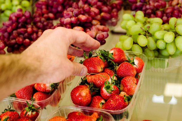 Mans hand choosig strawberries in grocery - 写真・画像