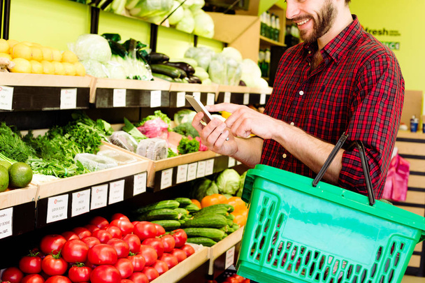 Caucasian man in red checkered shirt choosing vegetables in grocery - Photo, image