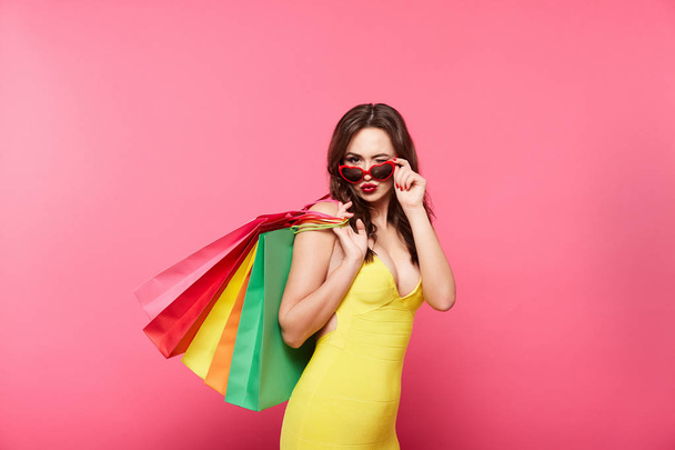 mujer joven con gafas de sol sosteniendo coloridas bolsas de compras sobre fondo rosa, compras y concepto de descuento
 - Foto, Imagen