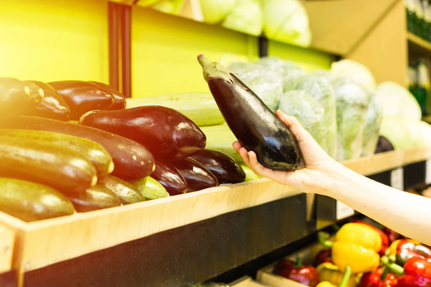 Womans hand choosing eggplants in grocery - 写真・画像