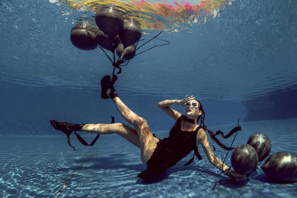 Underwater shoot of flying woman with black balloons - Foto, afbeelding
