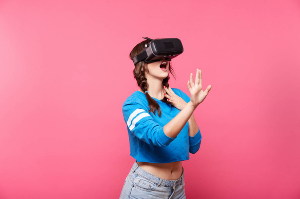 young woman with with virtual reality glasses posing at pink background, 3D, future concept - Foto, Imagem
