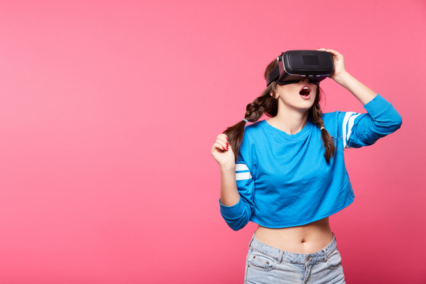 young woman with with virtual reality glasses posing at pink background, 3D, future concept - Zdjęcie, obraz