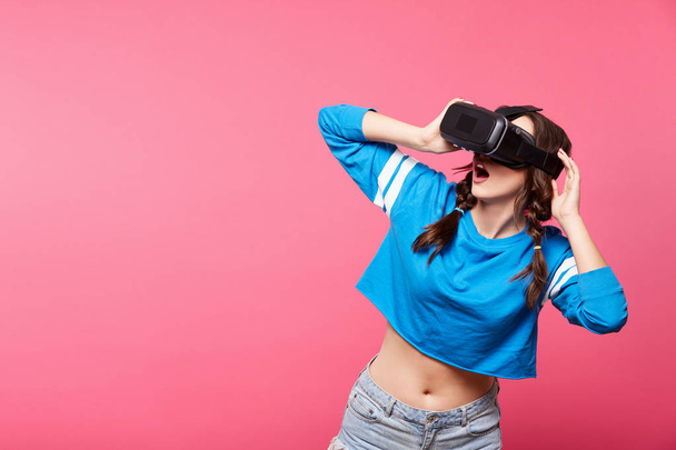 young woman with with virtual reality glasses posing at pink background, 3D, future concept - Photo, Image
