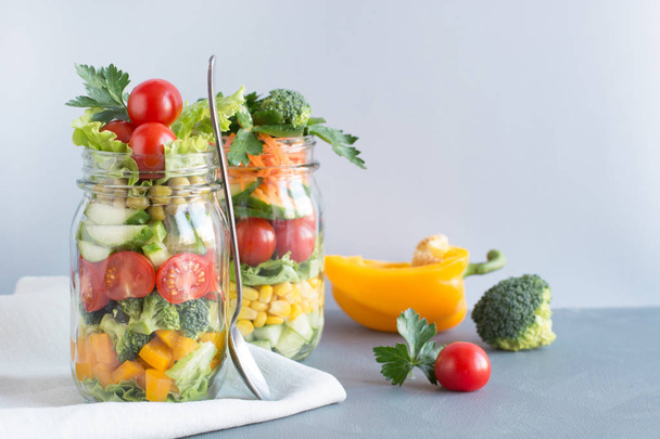 Vegetable healthy homemade detox colorful salad in mason jar with tomato, lettuce, broccoli on blue background. Copy space. Lunch for work. - Foto, Imagen
