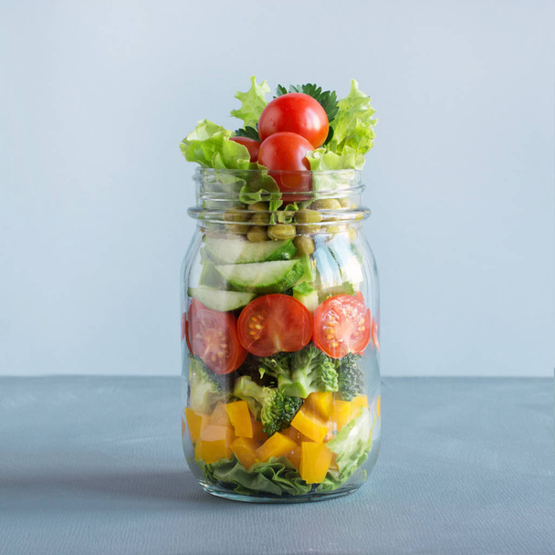 Healthy homemade vegetable salad in mason jar with tomato, lettuce, broccoli on blue. Copy space. Close up. Lunch for work. - Foto, Imagem