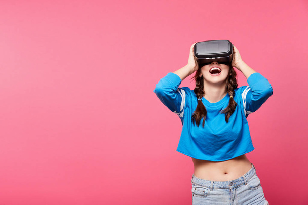 молодая женщина в очках виртуальной реальности позирует на розовом фоне, 3D, концепция будущего
 - Фото, изображение