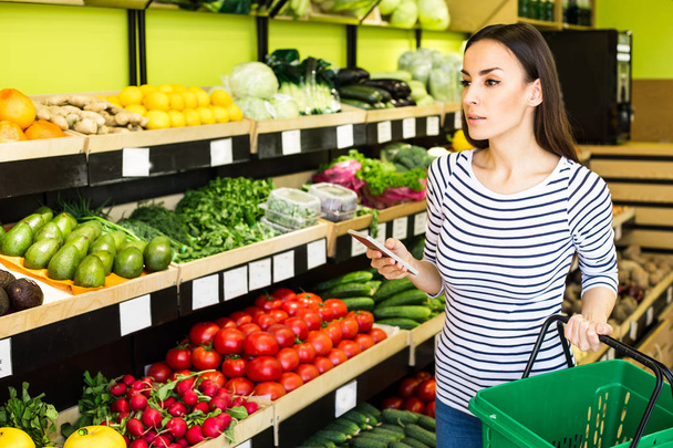 woman holding smartphone and checking buying list in supermarket - Φωτογραφία, εικόνα