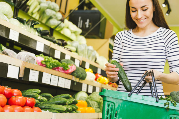 süpermarkette sepet içinde salatalık koyarak kadın - Fotoğraf, Görsel