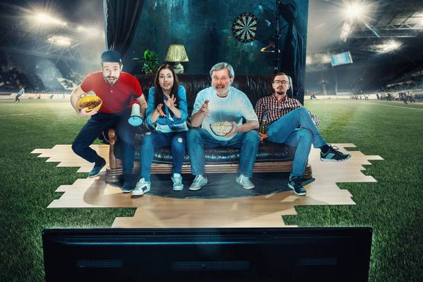 Soccer football fans sitting on the sofa and watching TV in the middle of a football field. - Zdjęcie, obraz