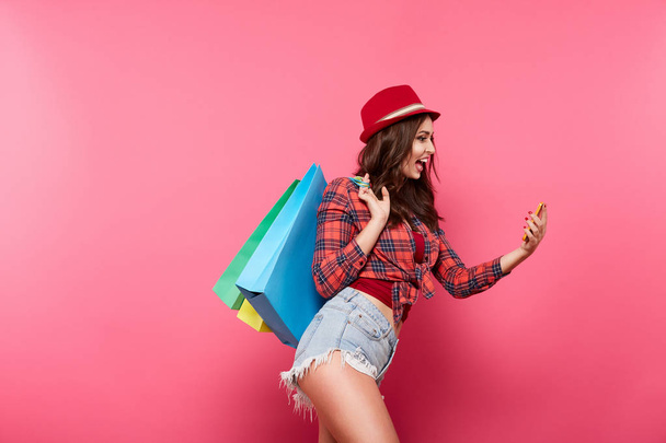 jeune femme heureuse avec des sacs à provisions colorés en utilisant le téléphone mobile sur fond rose, shopping et concept de réduction
 - Photo, image