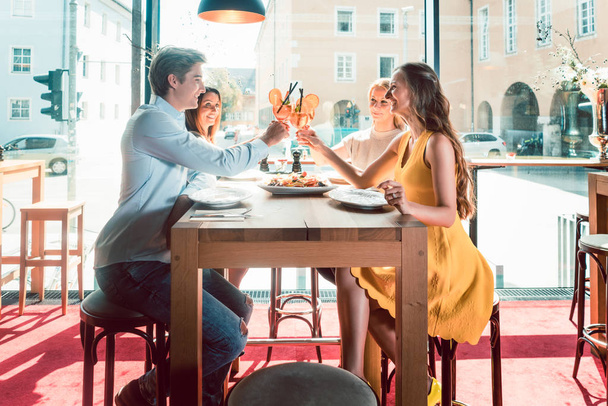 Jóvenes amigos brindando con cócteles antes de comer mariscos en un restaurante
 - Foto, Imagen