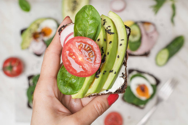 One sandwich with fresh summer tomato and avocado in female hand. Close up. Summer snack and superfood. - Foto, afbeelding
