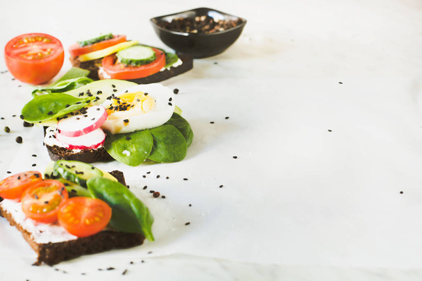 Different sandwiches with vegetables, eggs, avocado, tomato, rye bread on light marble table. Copy space, close up. Appetizer for party . - Foto, Bild