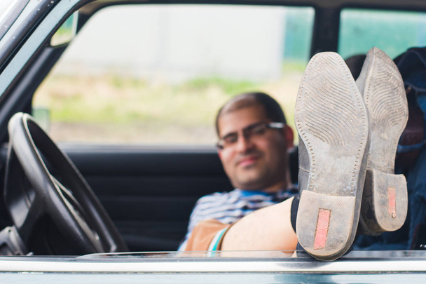 man resting in the car stretching his legs out of the car window - Photo, Image