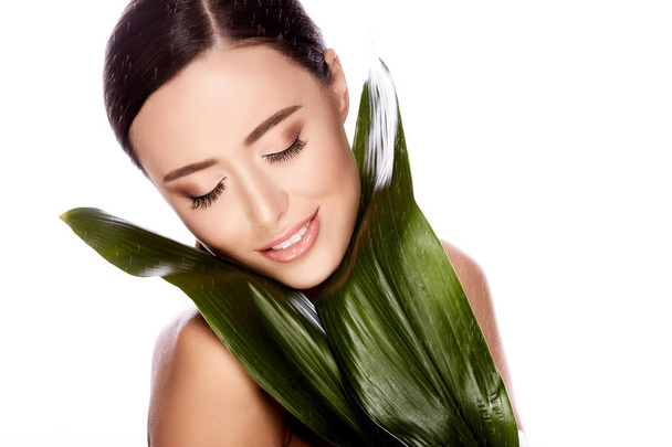 természetes és gyönyörű fiatal nő pózol zöld levelekkel elszigetelt fehér background, skin care koncepciót, hidratált bőr - Fotó, kép