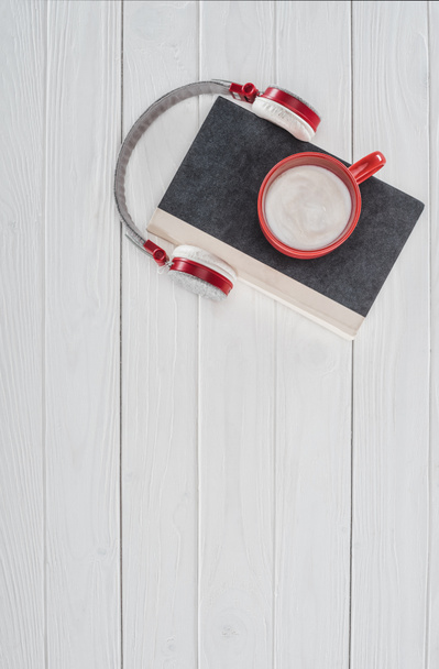 Draufsicht auf Buch, Kopfhörer und rote Tasse auf weißer Tischplatte - Foto, Bild