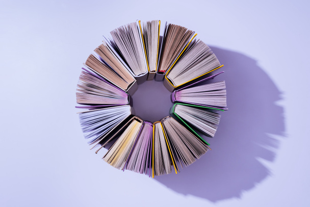 верхний вид стопки книг по кругу на фиолетовом столе
 - Фото, изображение