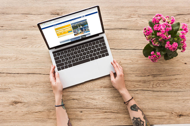 Teilansicht einer Frau am Tisch mit Laptop mit Bookingcom-Logo und Kalanhoe-Pflanze im Blumentopf - Foto, Bild