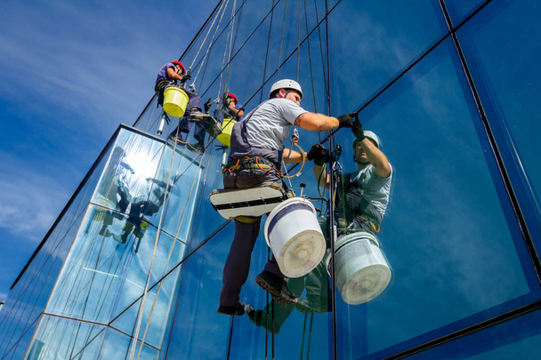 Промислові альпіністи застосовують силіконову гумову розв'язку серед скляного фасаду будівлі
. - Фото, зображення