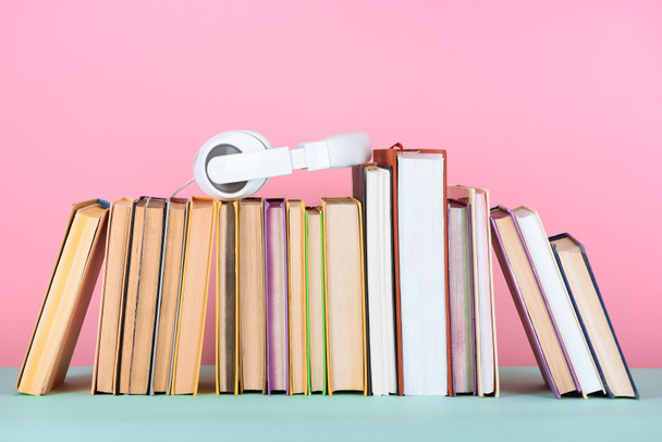 headphones on row of books on table on pink - Foto, Bild