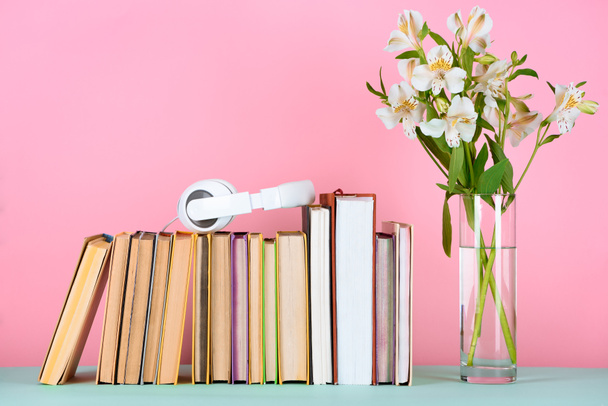 headphones on row of books and flowers in glass on table - Photo, Image