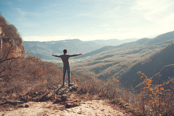 glücklicher junger Mann steht mit erhobenen Händen in den Bergen - Foto, Bild