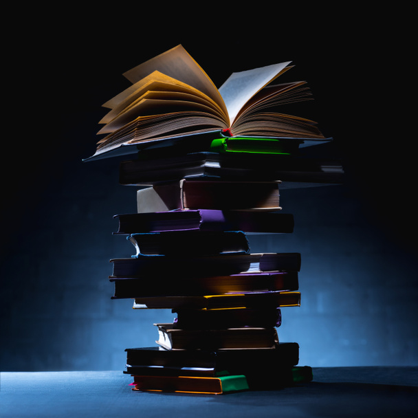 Stapel farbiger Bücher mit offenem Buch auf dunkler Oberfläche - Foto, Bild