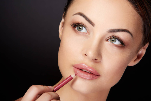 concepto de belleza, mujer joven pintando labios con lápiz labial rojo, fondo negro
 - Foto, Imagen
