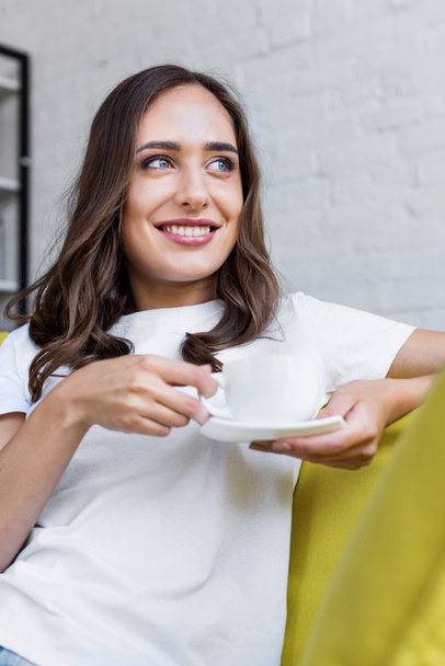 happy young woman holding cup of coffee and looking away at home - Photo, Image