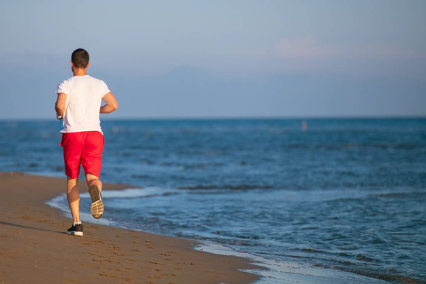 Vue arrière de l'homme faisant du jogging sur la plage contre la mer bleue et le ciel
 - Photo, image