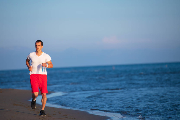 Vue de face de l'homme faisant du jogging sur la plage contre la mer bleue et le ciel
 - Photo, image