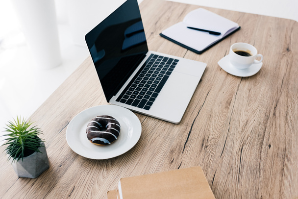 closeup view of laptop with blank screen, doughnut, coffee cup, potted plant and textbooks  - Fotó, kép