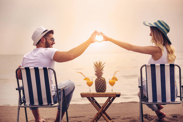 Молода пара розслабляє і п'є коктейлі на піщаному пляжі на заході сонця
 - Фото, зображення