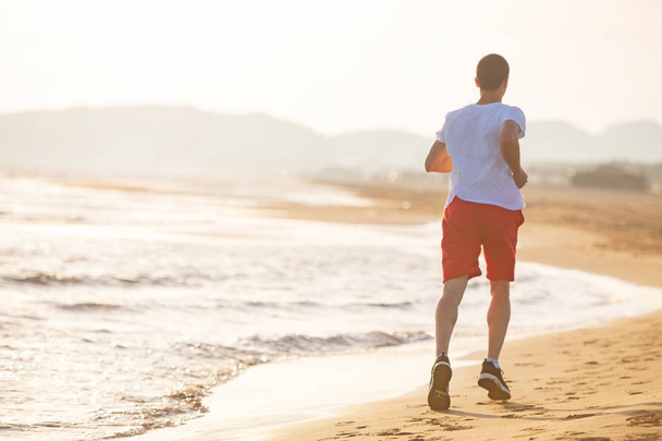 Täyspitkä peruutuskuva miehestä juoksemassa rannalla auringonlaskun aikaan
 - Valokuva, kuva