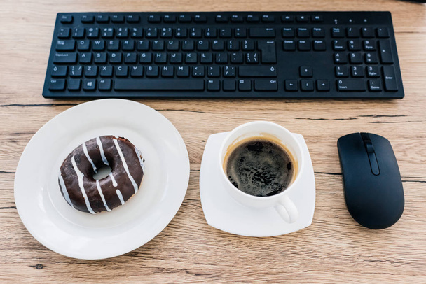 top view of doughnut, coffee cup, computer mouse and computer keyboard on wooden table  - Фото, изображение