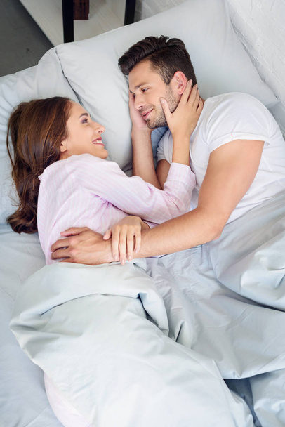 young smiling couple hugging and looking at each other while relaxing in bed - Foto, imagen