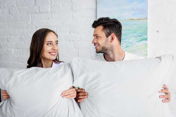 attractive girlfriend and happy boyfriend sitting on bed with pillows - Foto, Imagen