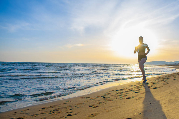 Front view of healthy young fit woman running on sunrise seaside trail - Fotó, kép