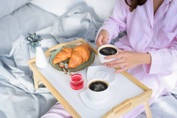 bijgesneden beeld van de vrouw in roze pyjama ontbijten in bed - Foto, afbeelding