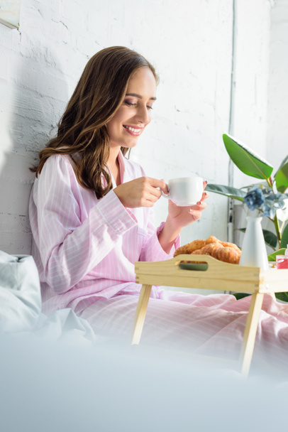 beautiful smiling woman in pink pajamas drinking coffee for breakfast in bed - Фото, изображение