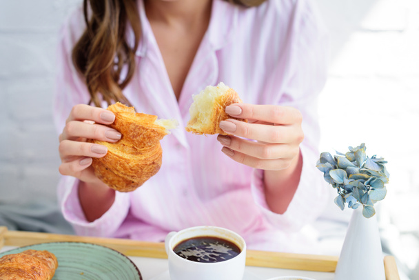 частичный вид женщины в пижаме с круассаном и кофе на завтрак
 - Фото, изображение