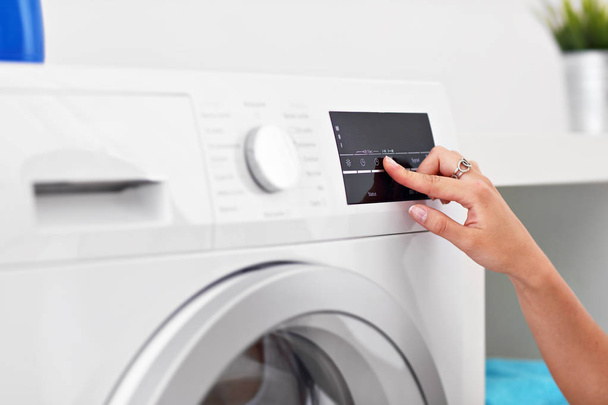 Porträt einer jungen Hausfrau mit Wäsche neben Waschmaschine - Foto, Bild