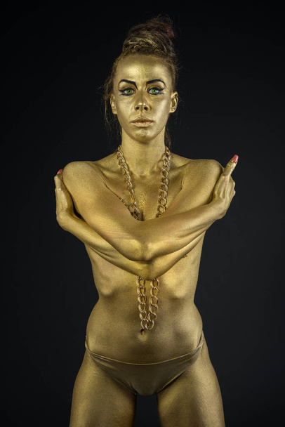 woman fully dressed in gold and font type in artistic position and  on black background - Zdjęcie, obraz
