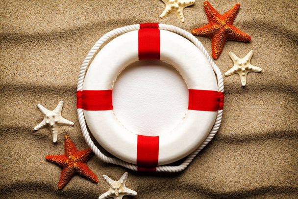 Summer background - lifebuoy and various starfish on the beach - Foto, afbeelding