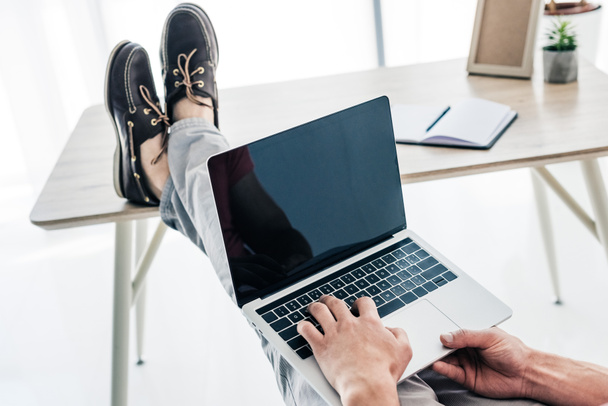 partial view of man holding legs on table and typing on laptop  - Photo, Image