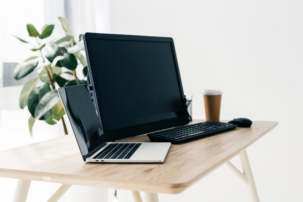 vista frontal del lugar de trabajo con computadora portátil, computadora, taza de papel de café en la mesa y la planta en maceta
  - Foto, imagen