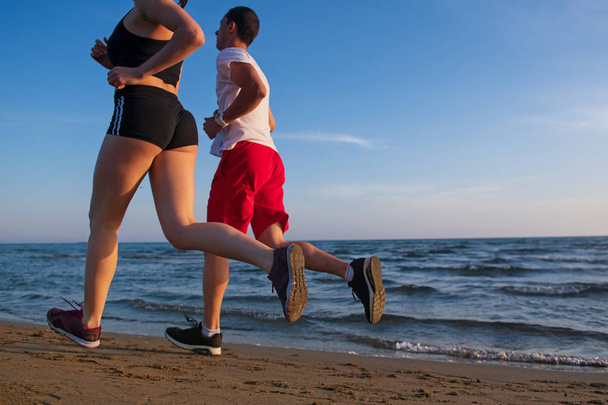 Vista de sección baja de pareja joven corriendo en la playa tropical al atardecer
 - Foto, Imagen