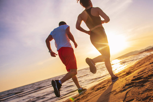 Visão traseira de homem e mulher correndo juntos pela praia tropical ao pôr do sol
 - Foto, Imagem